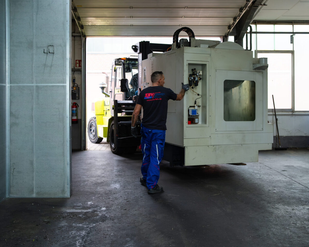 Mitarbeiter begleitet eine Maschine beim Einfahren in eine Halle mit Gabelstapler.