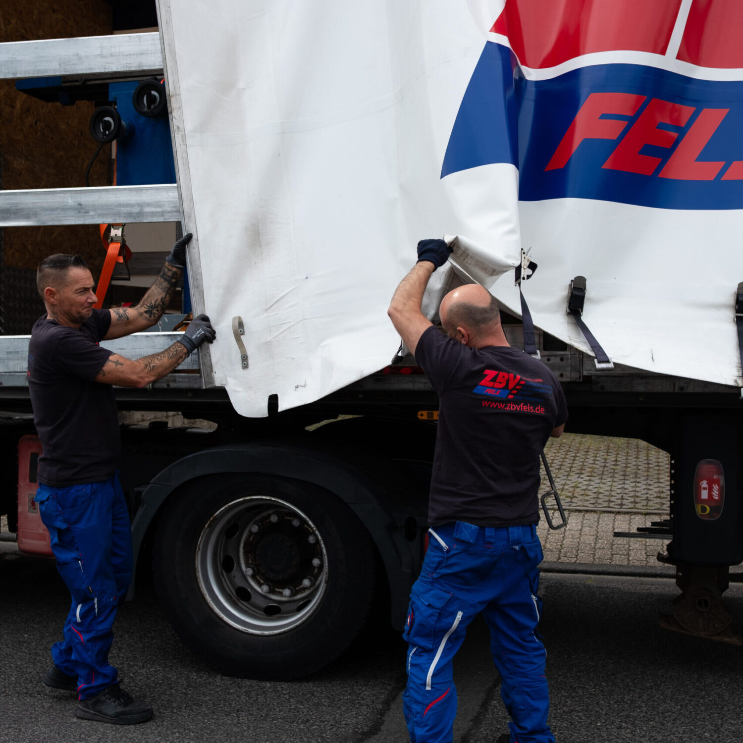 Zwei Mitarbeiter von ZBV Fels öffnen die Plane eines Lkw-Aufliegers.