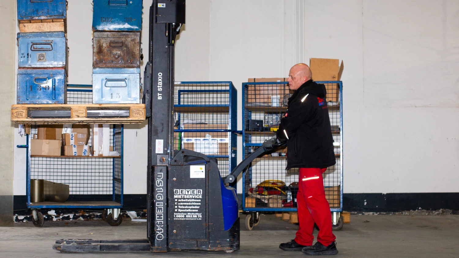 Mitarbeiter von ZBV Fels heben Metallboxen mit einem Elektrohubwagen.