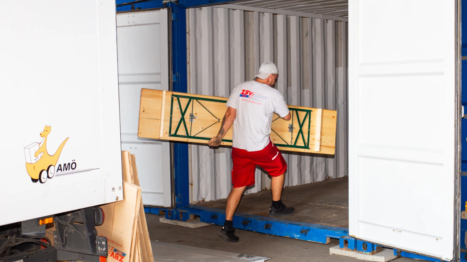 Mitarbeiter von ZBV Fels trägt ein zusammengeklapptes Holzmöbel in einen Selfstorage-Container.