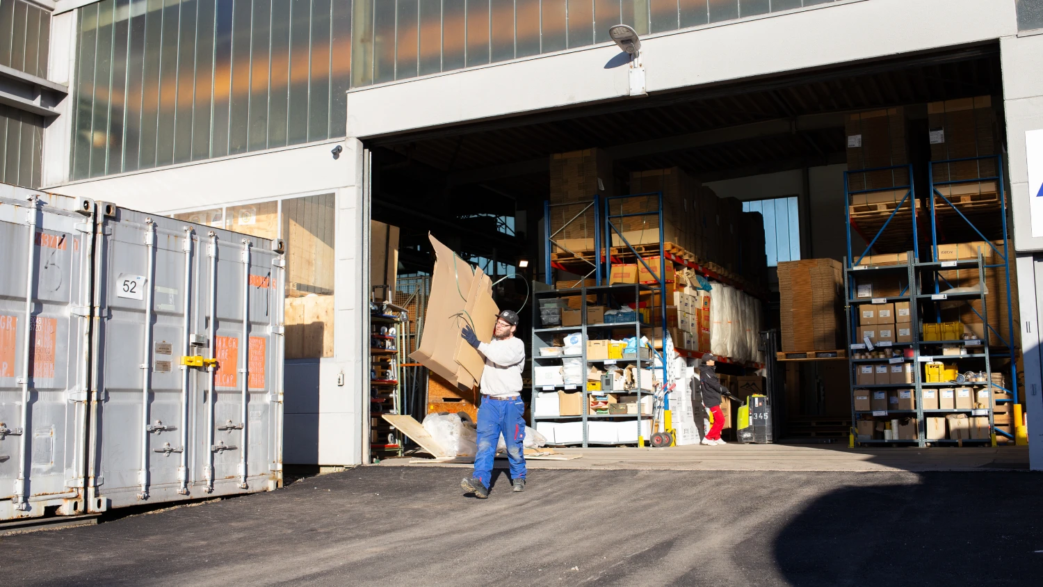 Mitarbeiter von ZBV Fels transportieren Verpackungsmaterial vor einem Industriegebäude.