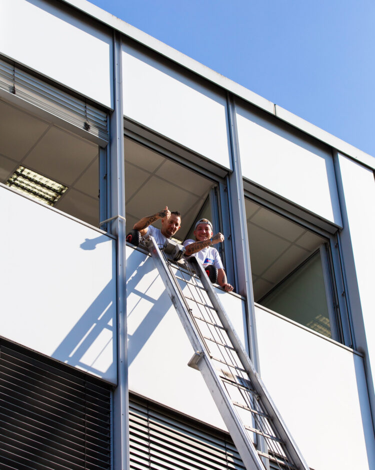 Zwei Mitarbeiter von ZBV Fels halten den Daumen aus dem Fenster.