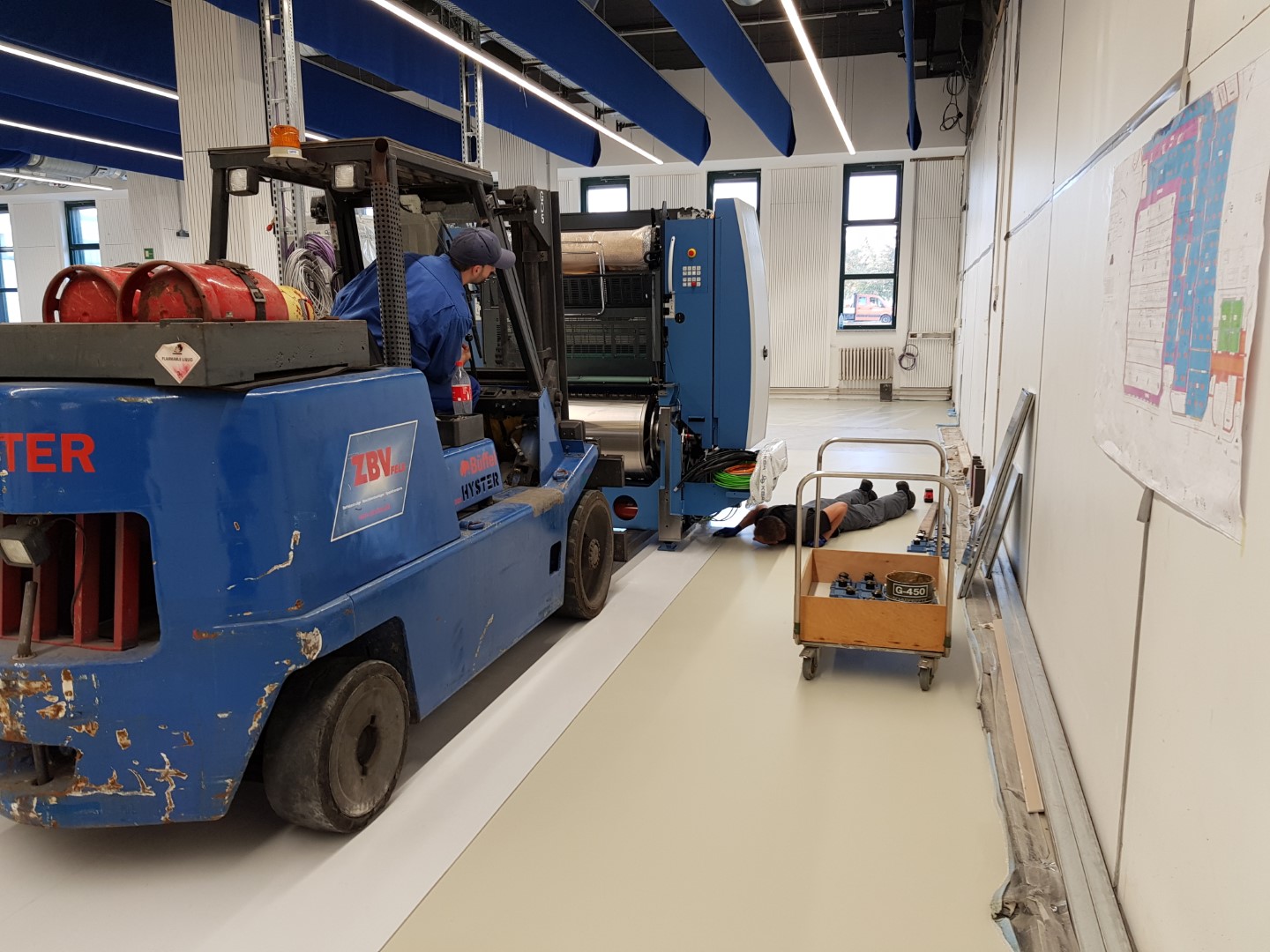 Gabelstapler in einer Werkstatt, zwei Personen arbeiten an einer Maschine.