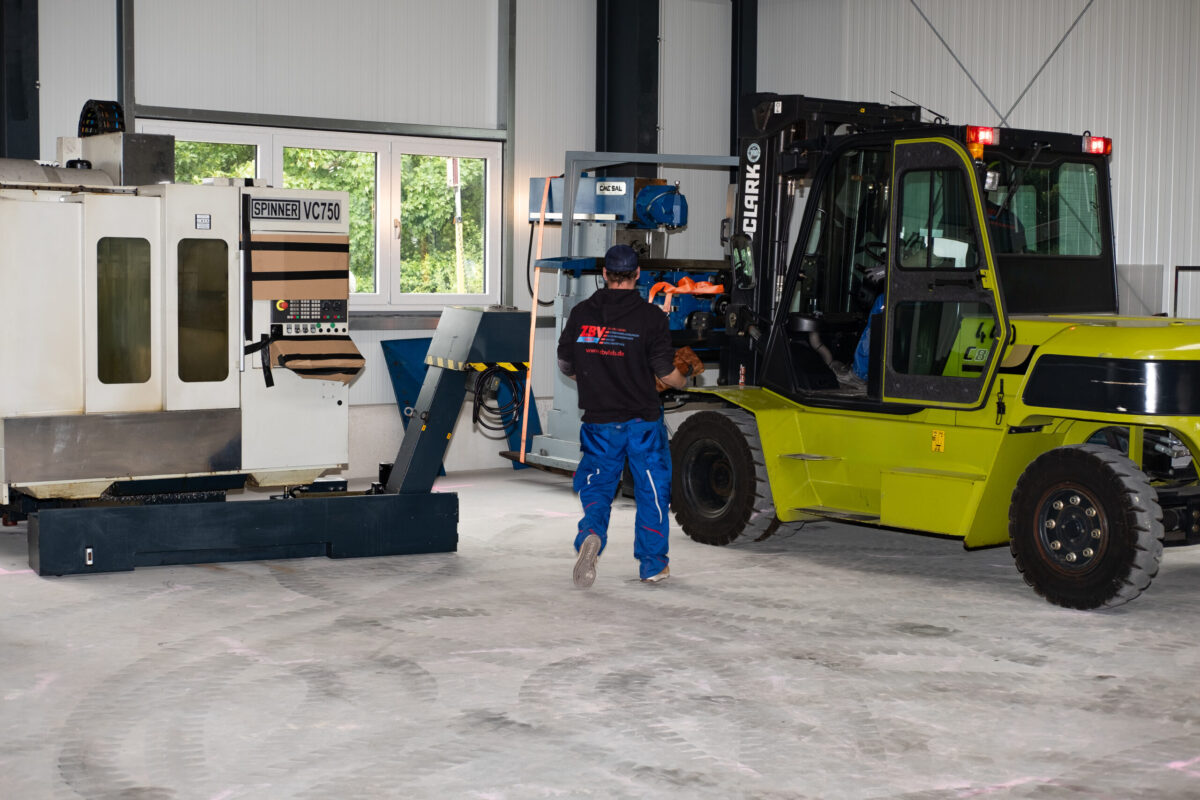 Mitarbeiter in einer Halle mit Gabelstapler und Industriemaschine.