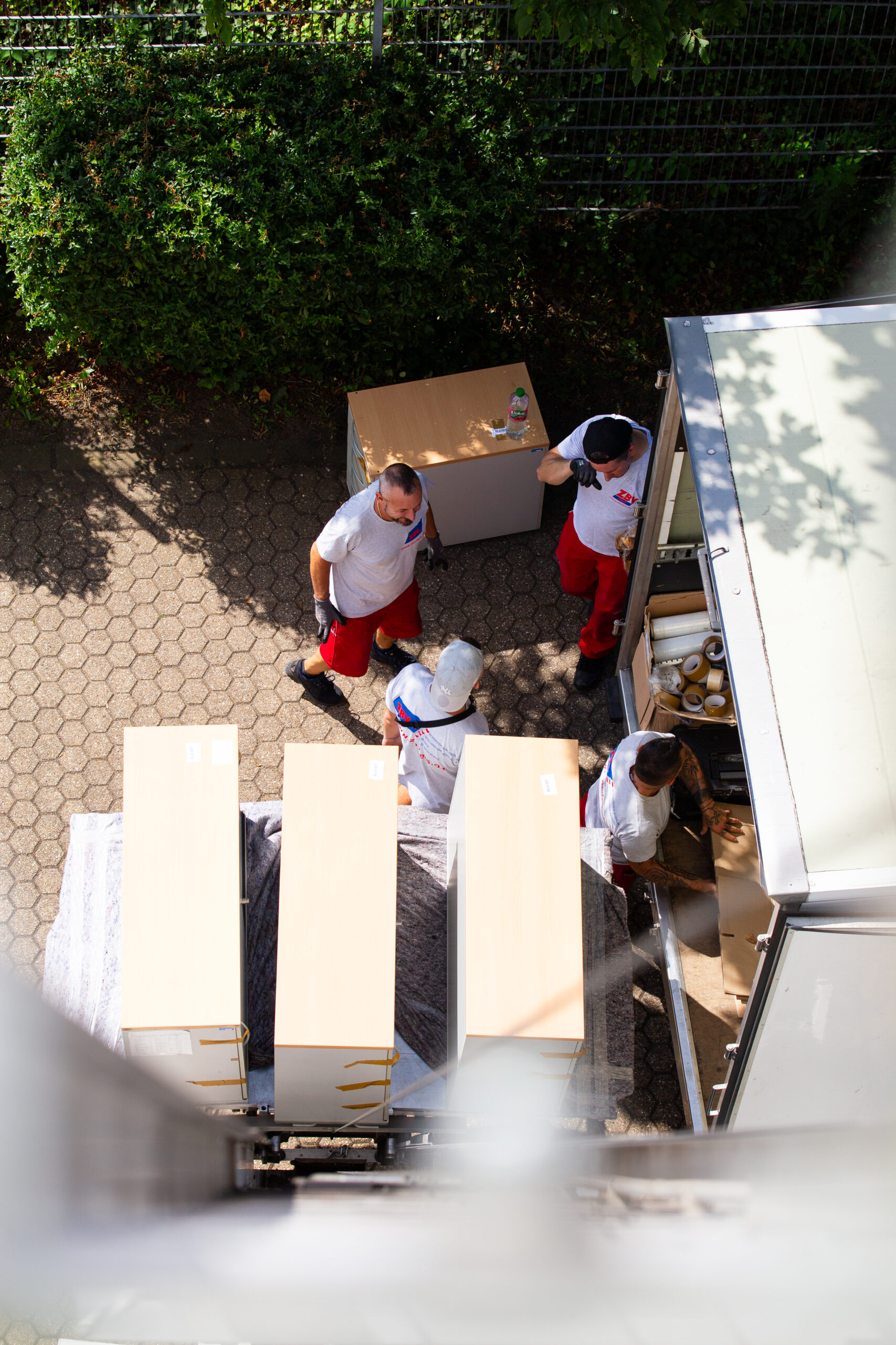 Luftaufnahme: Das Umzugsteam von ZBV Fels verlädt Möbel mit Schutzmaterial in einen Transporter.