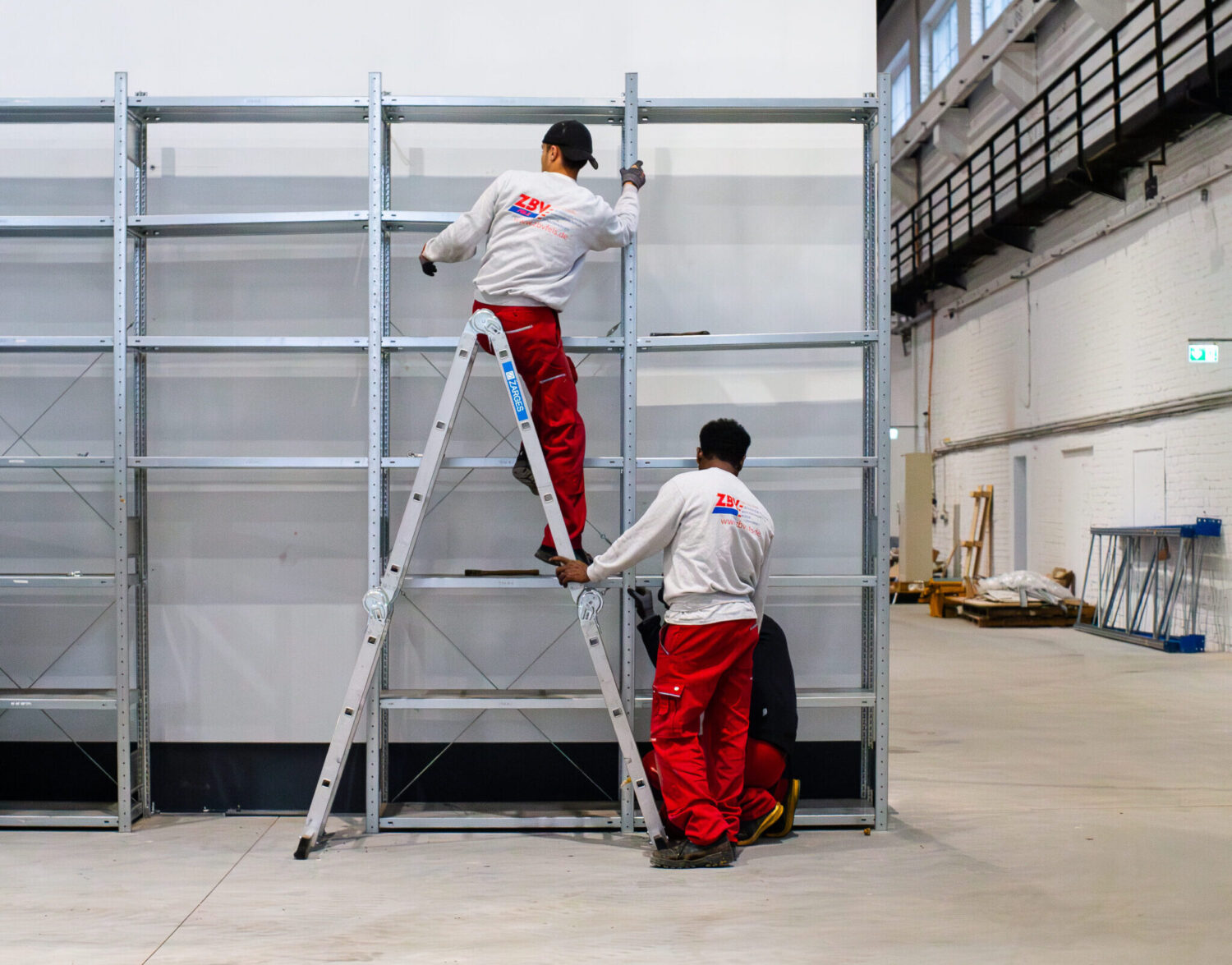 Team von ZBV Fels baut große Metallregale in einer Lagerhalle auf.
