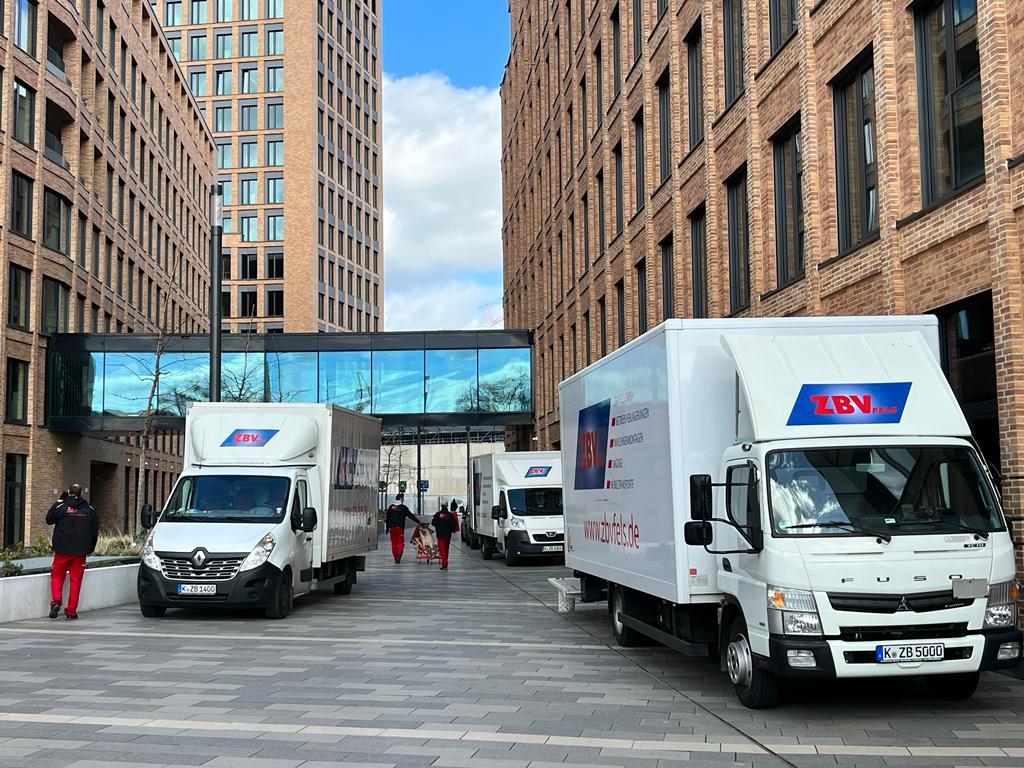 Zwei Lieferwagen stehen in einer Stadtstraße zwischen hohen Backsteinhäusern.